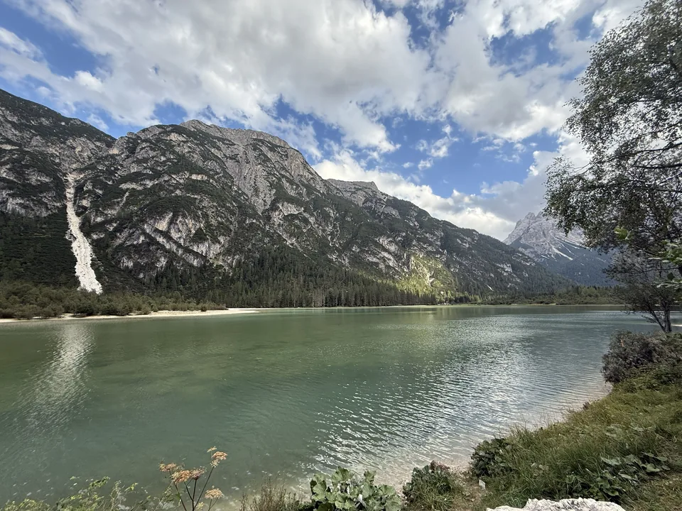 Grüner Bergsee vor bewaldeten Hängen und steilen Felswänden